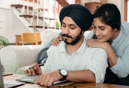 Peer-to-Peer Support Networks - Cheerful ethnic couple using calculator while sitting at table