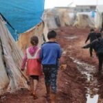 Flood-Prone Areas - Children walking on dirty street with tents