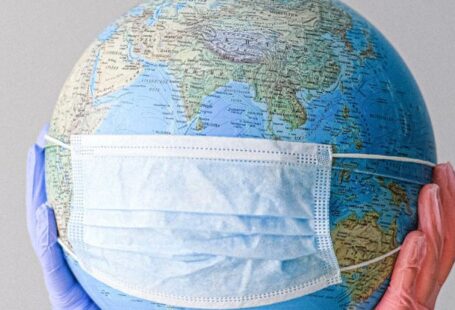 Pandemic - Hands With Latex Gloves Holding a Globe with a Face Mask