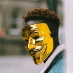 Urban Policy - Black activist in golden Anonymous mask standing on city street
