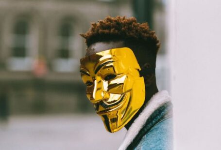Urban Policy - Black activist in golden Anonymous mask standing on city street