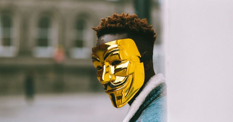 Urban Policy - Black activist in golden Anonymous mask standing on city street