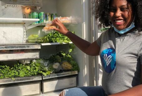 Food Banks - A black female activist looking at camera next to a food bank 